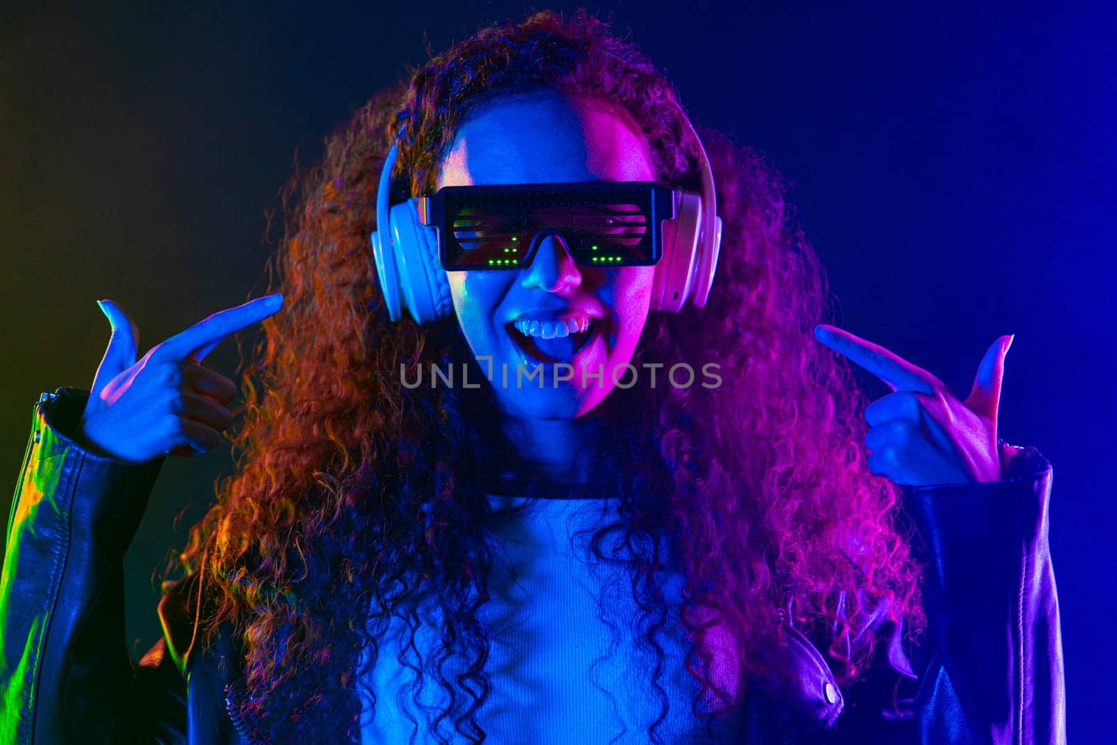 Positive woman listening music, enjoying with headphones in neon colorful studio. Radio, wireless modern sound technology, online player. High quality photo