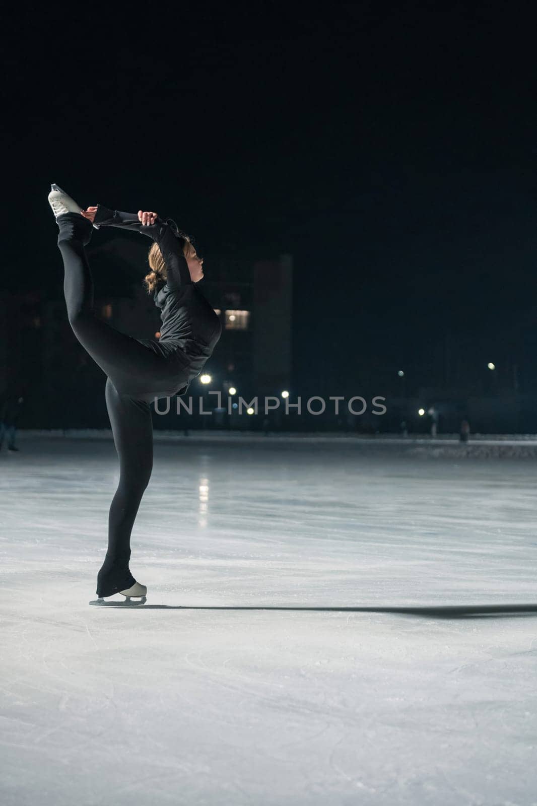 Beautiful young woman ice skating and performing short program over city outdoor ice arena. Winter activities concept
