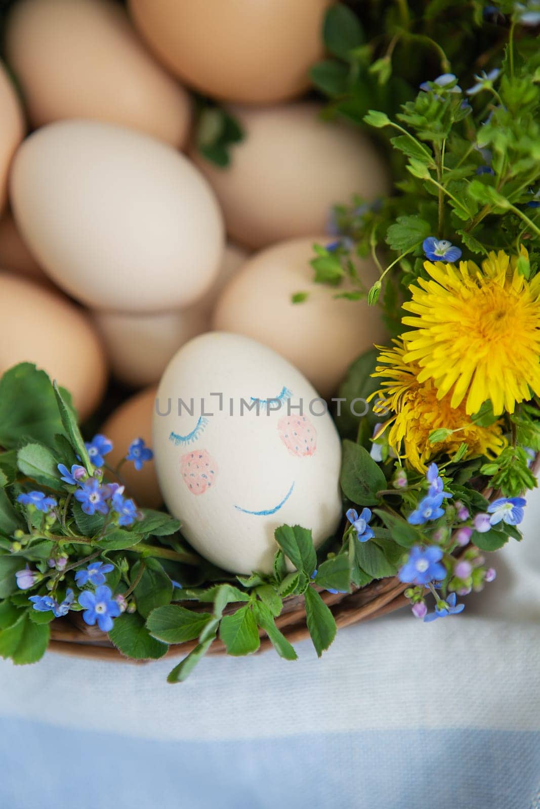 Beautiful spring bouquet in a wooden basket with Easter painted eggs, eggs with cute faces. Colorful greeting card for the Easter holiday