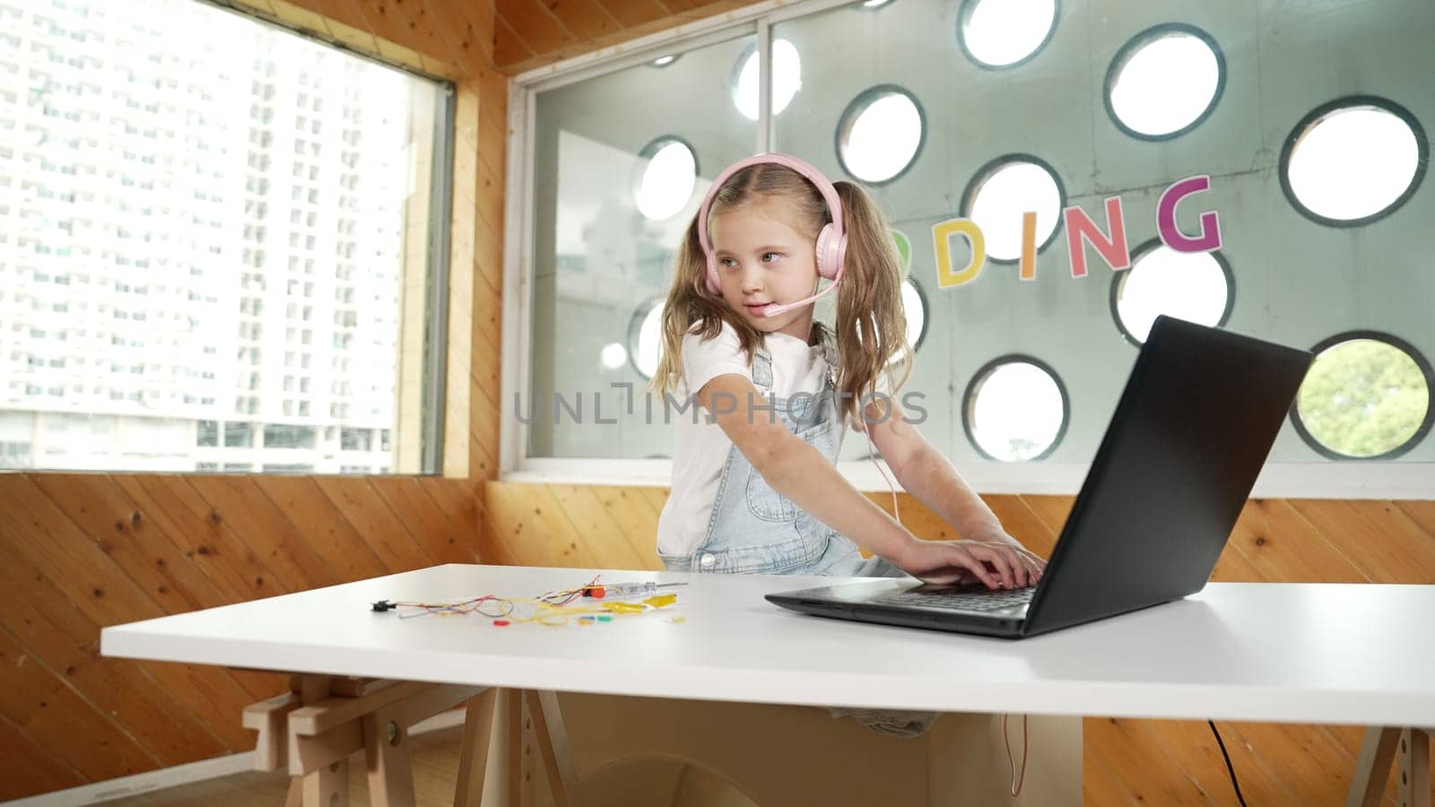 Smart caucasian girl wearing headphone and looking at electronic equipment. Skilled student working by using laptop to searching and learning electric equipment on table. Smart classroom. Erudition.