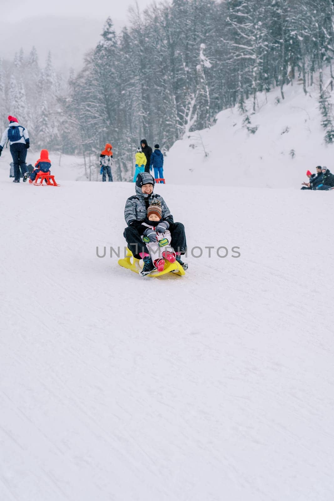 Smiling mother with a small child goes down the slope of a snowy mountain on a sled. High quality photo