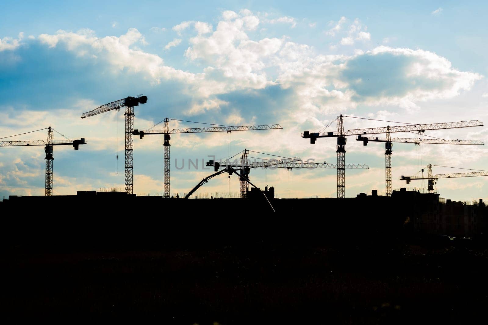 Industrial construction cranes and building silhouettes over sun at sunrise. by DovidPro