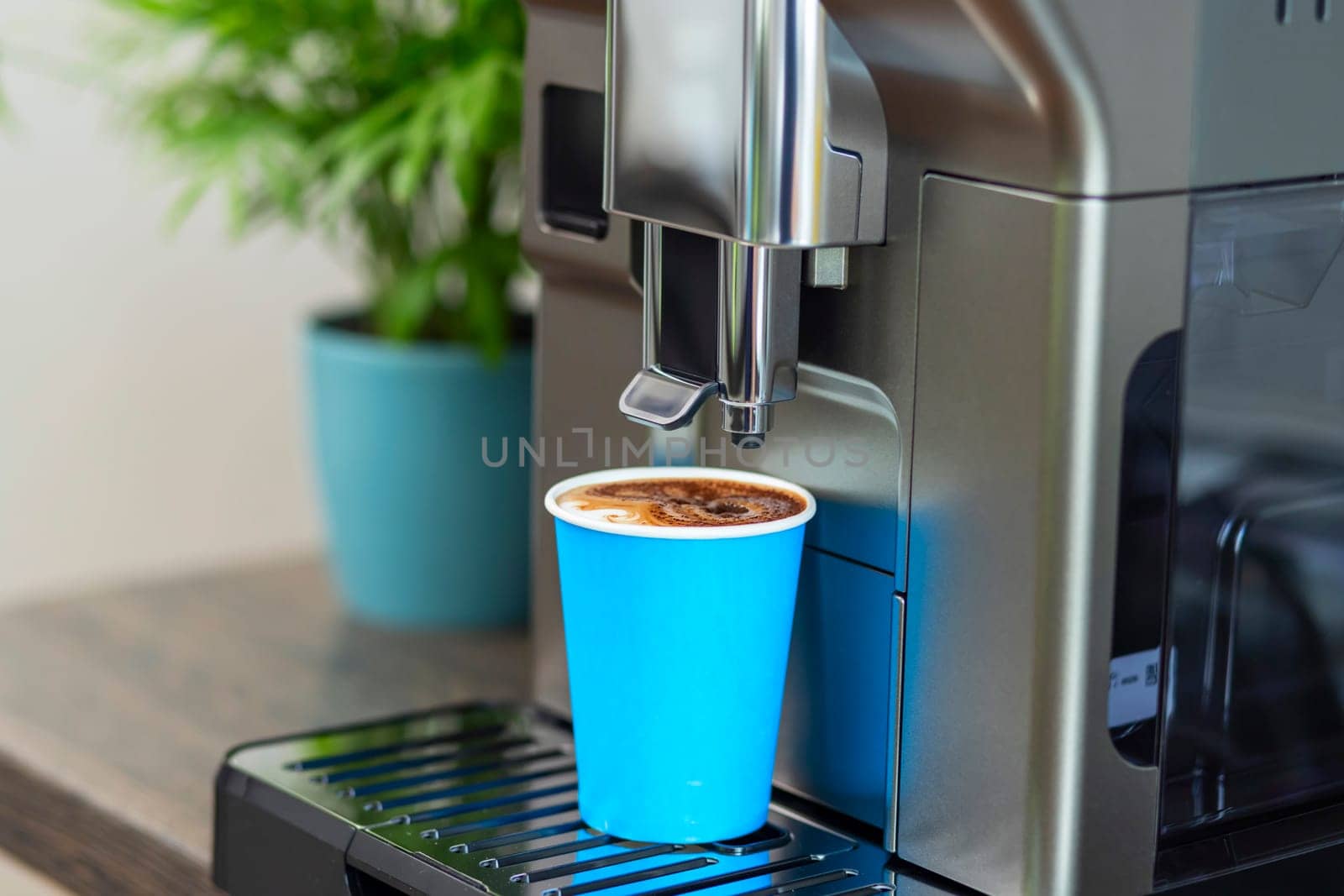 Close-up view of an automatic espresso machine serving fresh coffee in a vibrant blue cup, placed on a kitchen counter.