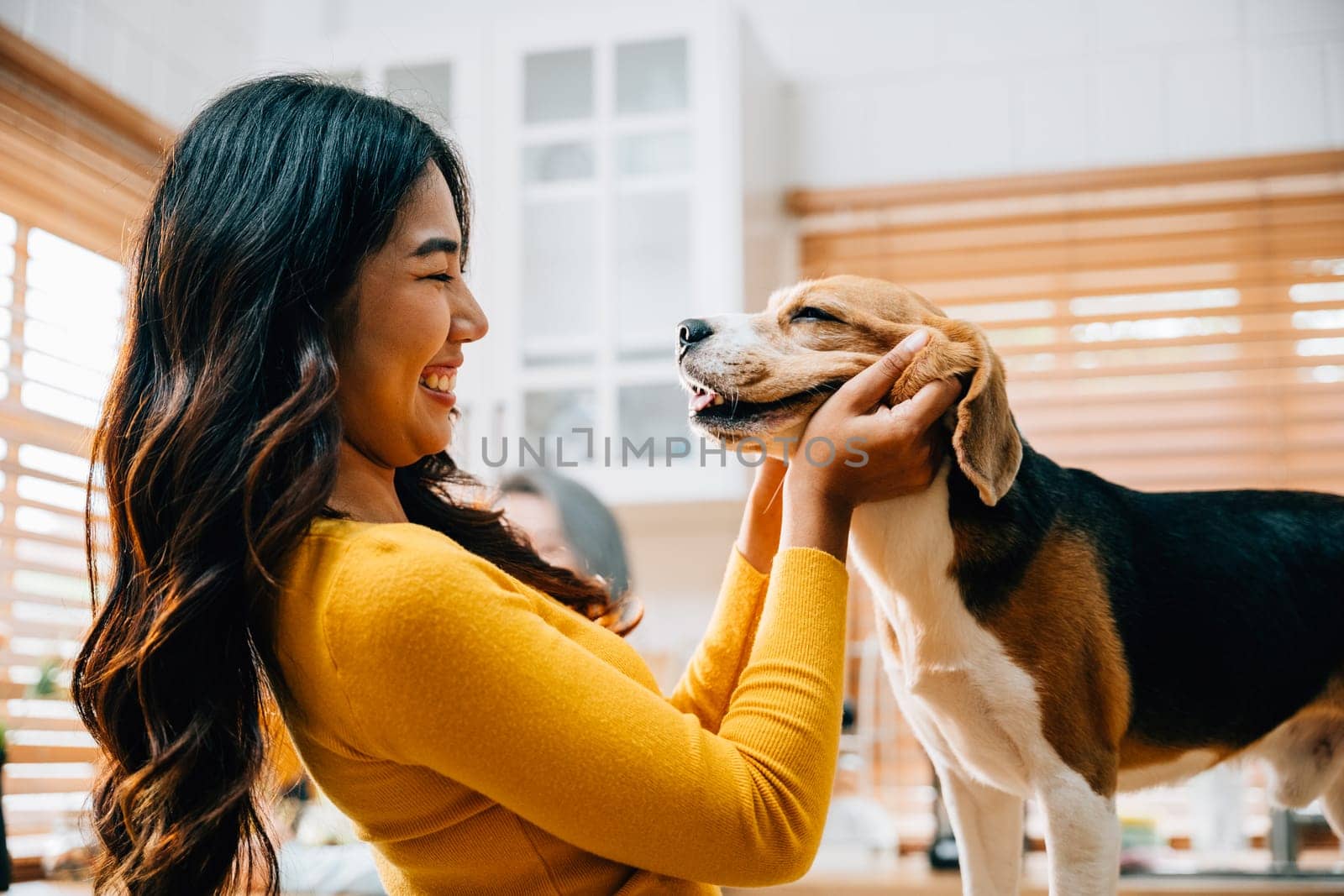 With her Beagle, an Asian woman embraces the kitchen as a place of happiness and play. Their joyful interaction exemplifies the care, togetherness, and family enjoyment of having a pet. Pet love by Sorapop