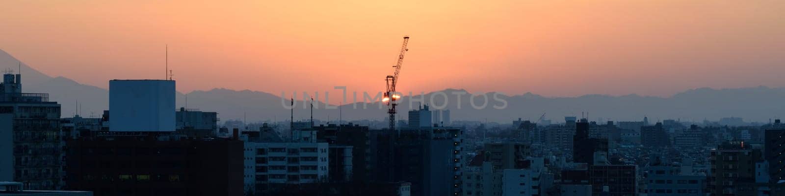 Panoramic city skyline at sunset with silhouettes of buildings and a vibrant orange sky.
