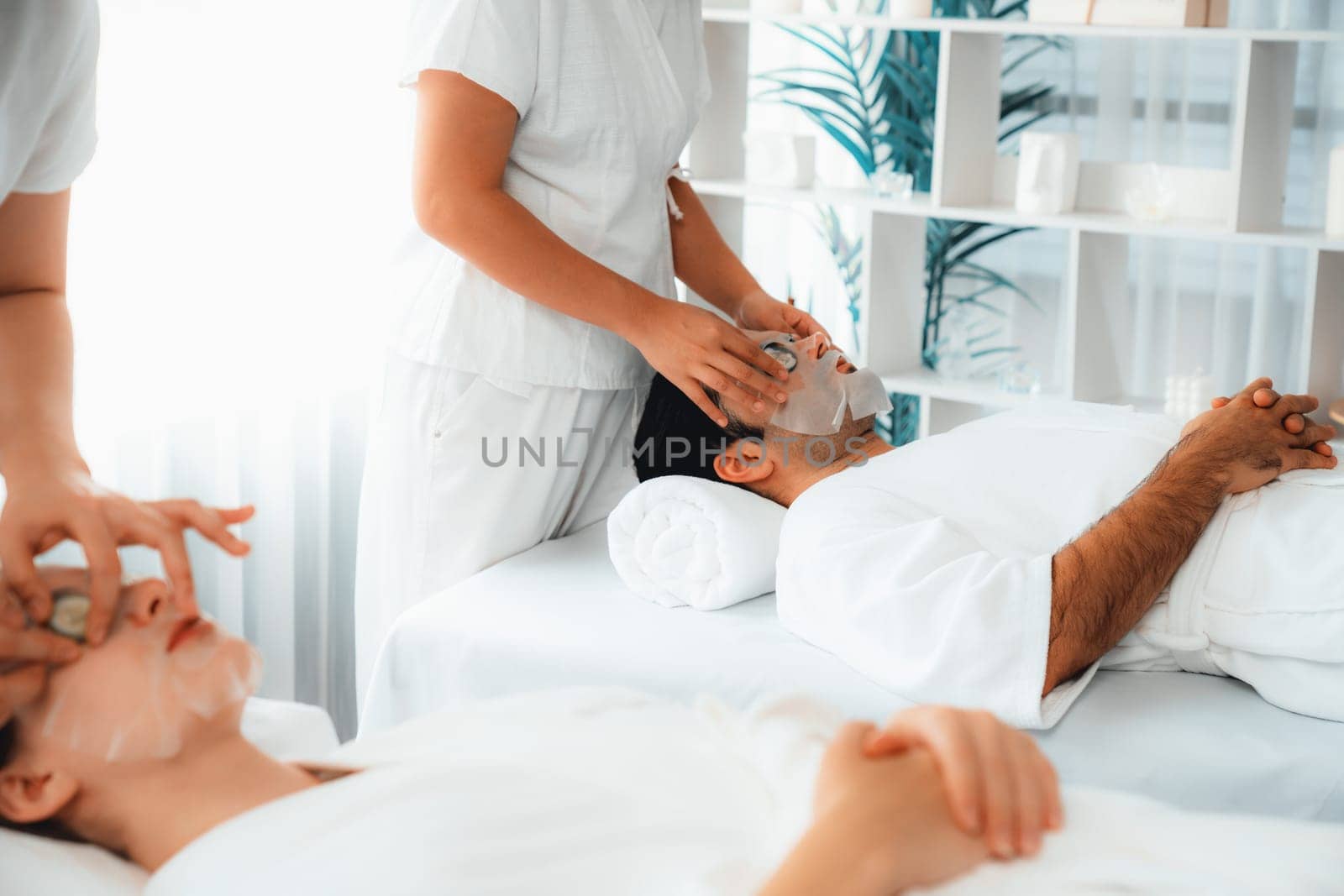 Serene daylight ambiance of spa salon, couple customer indulges in rejuvenating with luxurious cucumber facial mask. Facial skincare treatment and beauty care concept. Quiescent