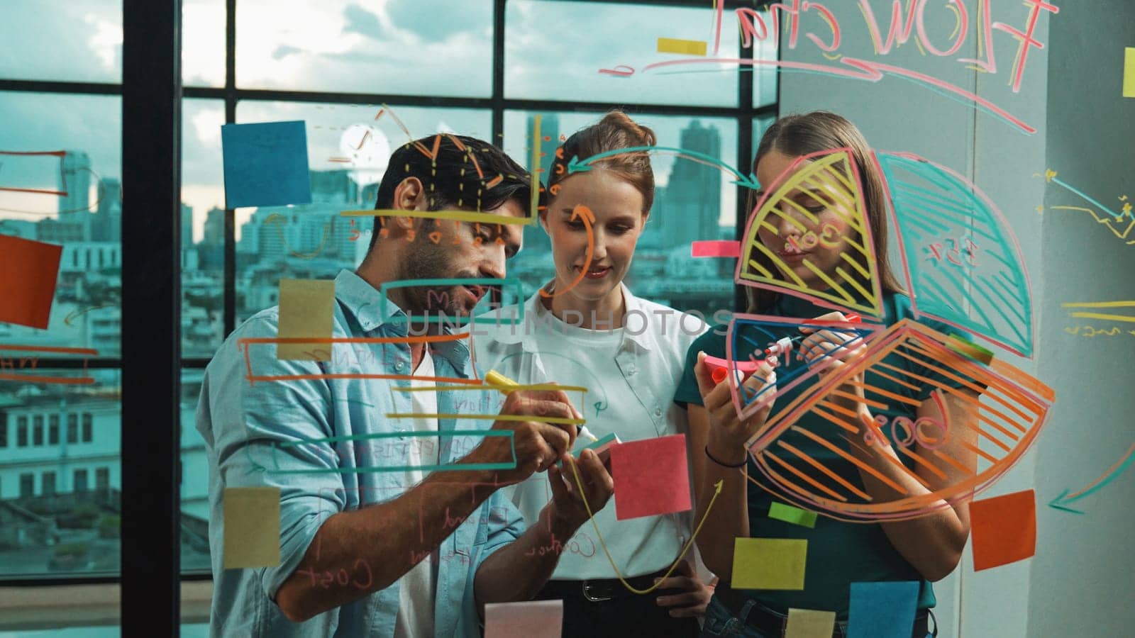 Group of happy professional business team working together, discussing and writing at sticky notes about marketing idea, plan, strategy at glass wall with graph and colorful sticky notes. Tracery