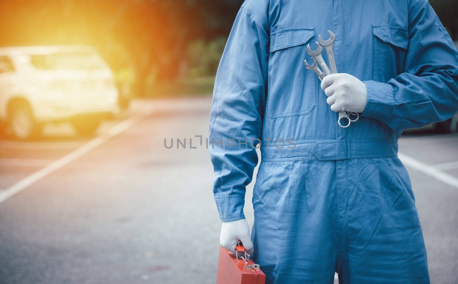 Skilled car mechanic at work on the road, holding a large wrench with hands clad in blue workwear. Close-up shot of the hands.