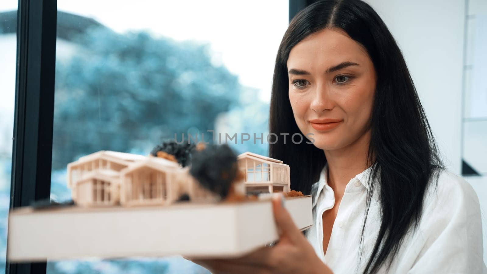 Close up of skilled young beautiful caucasian architect lift house model left side and right sight to check and focus on inspecting mistake point at modern office with blueprint. Immaculate.