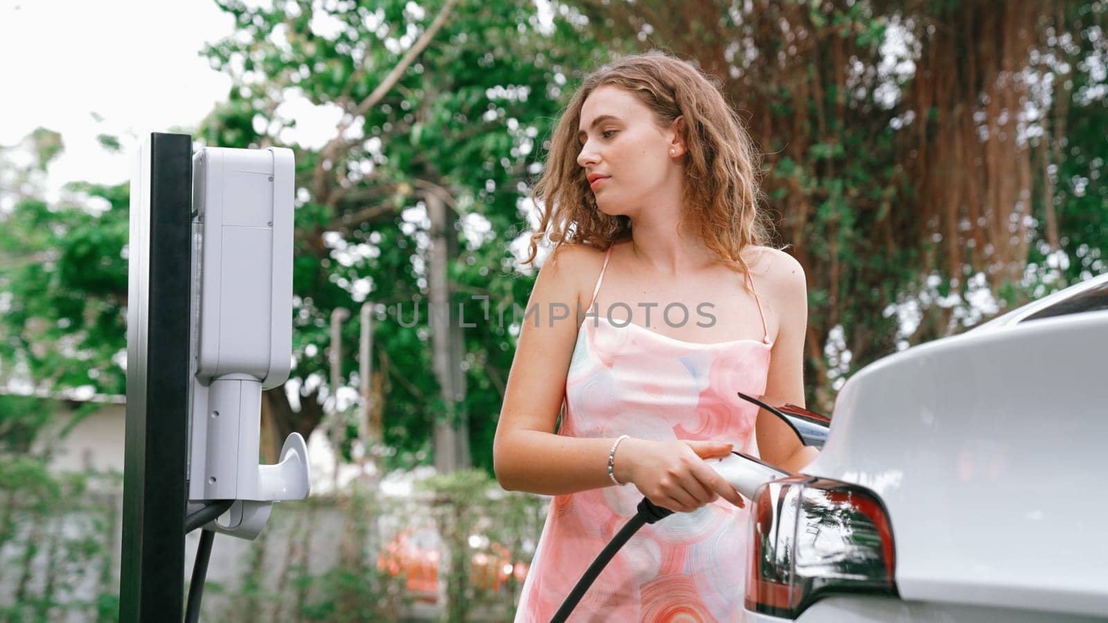 Closeup woman recharge EV electric car's battery at parking lot in natural green park. Clean energy technology for rechargeable vehicle for sustainable and eco friendly travel. Synchronos