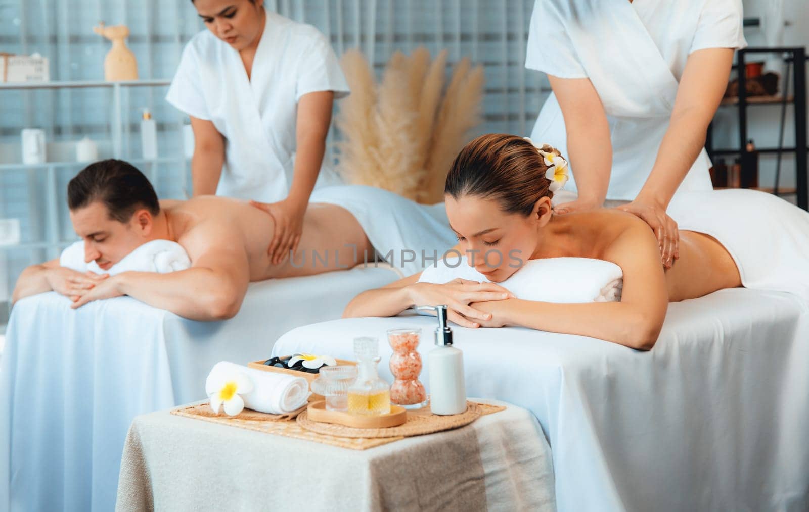 Caucasian couple customer enjoying relaxing anti-stress spa massage and pampering with beauty skin recreation leisure in day light ambient salon spa at luxury resort or hotel. Quiescent
