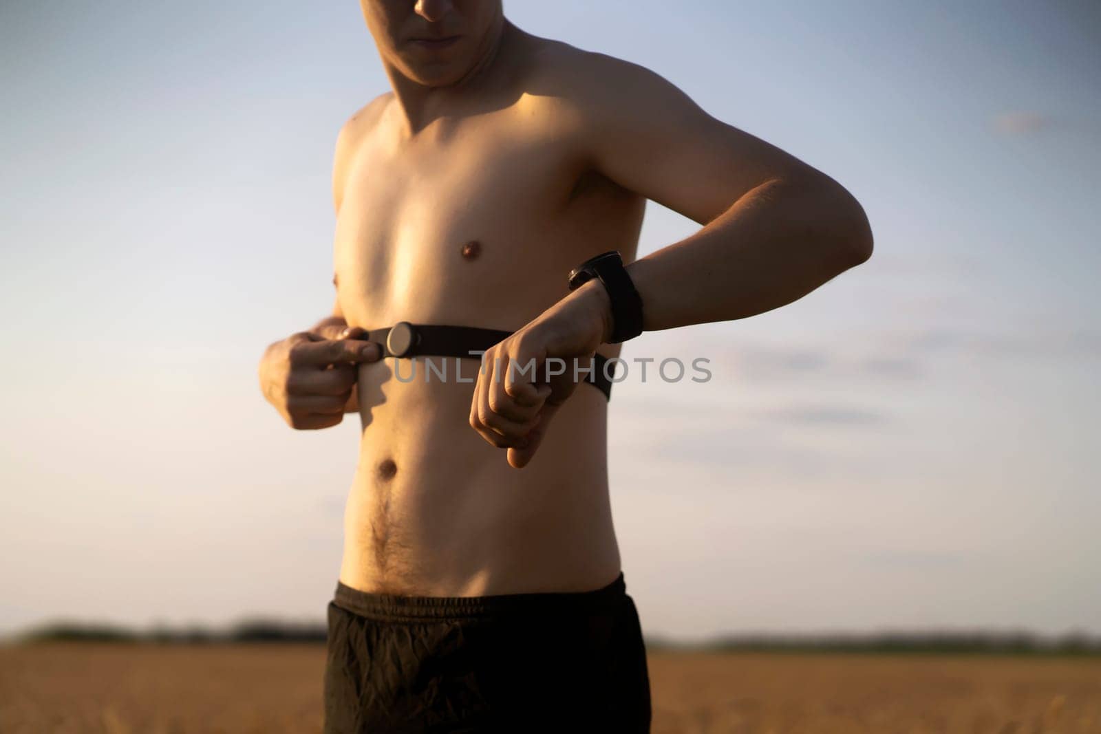 An athletic young man warms up outdoors, puts on a heart rate monitor and prepares for an active run, a person leads a healthy lifestyle and competently approaches running training.