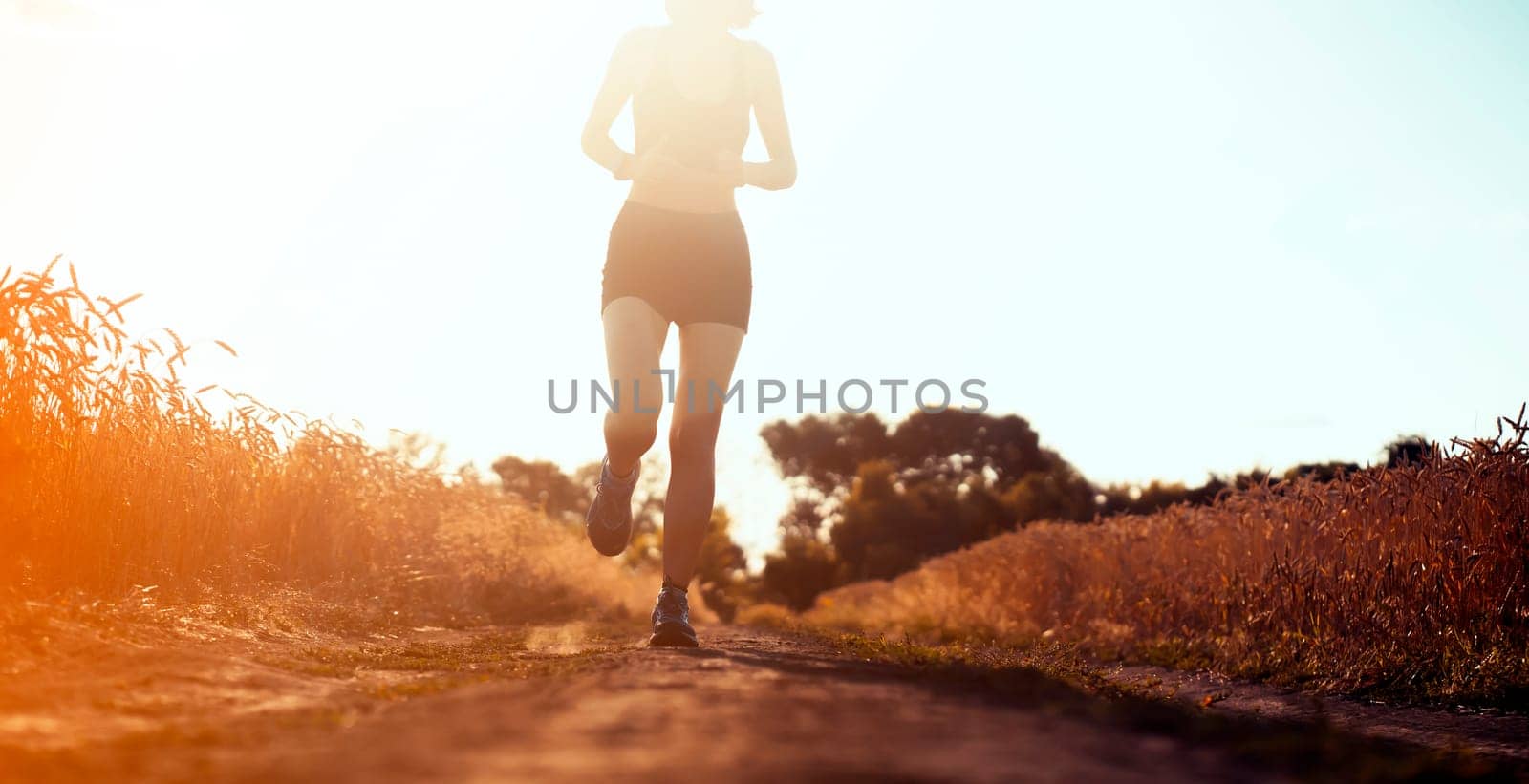 Young sports girl in a top and shorts trains outdoors, runs at sunset. A woman is engaged in trail running outdoor, preparing for a long race, enjoys an active lifestyle.