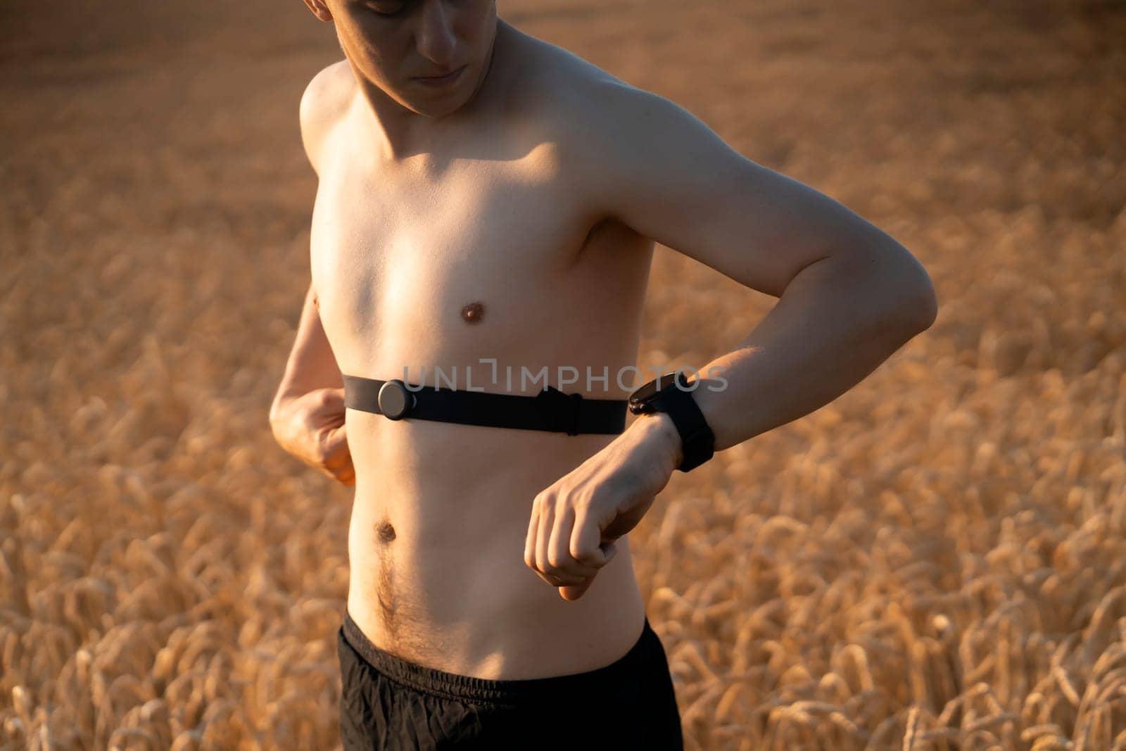 An athletic young man warms up outdoors, puts on a heart rate monitor and prepares for an active run, a person leads a healthy lifestyle and competently approaches running training.
