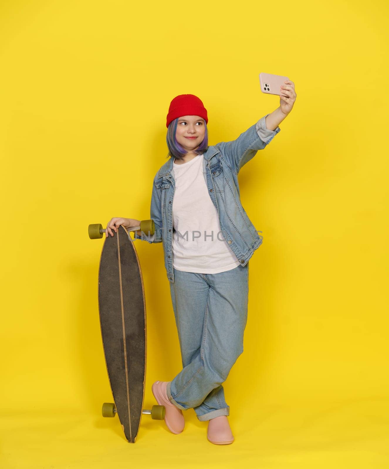 Stylish Teen With Longboard Make Selfie, Girl In Red Hat With Skateboard And Mobile Phone On Yellow Background. Teenager Immersed In Contemporary Lifestyle Of Skateboarding And Digital Connectivity. by LipikStockMedia
