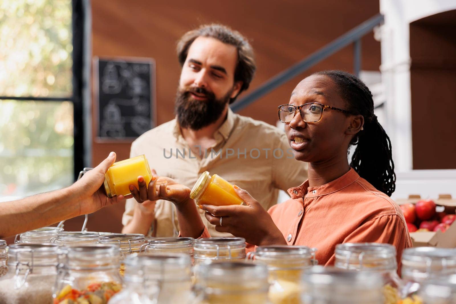 Portrait of multiracial customers actively selecting bio food items at local small business. Boyfriend and girlfriend shopping for natural honey in an eco friendly convenience store.