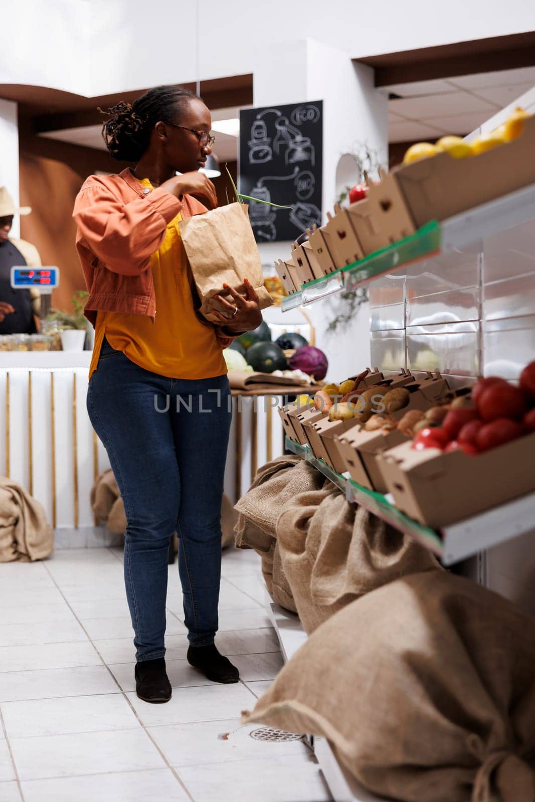 A youthful black woman choosing bulk organic products, using reusable bags. Image showing an African American female customer looking for a variety of fruits and vegetables.