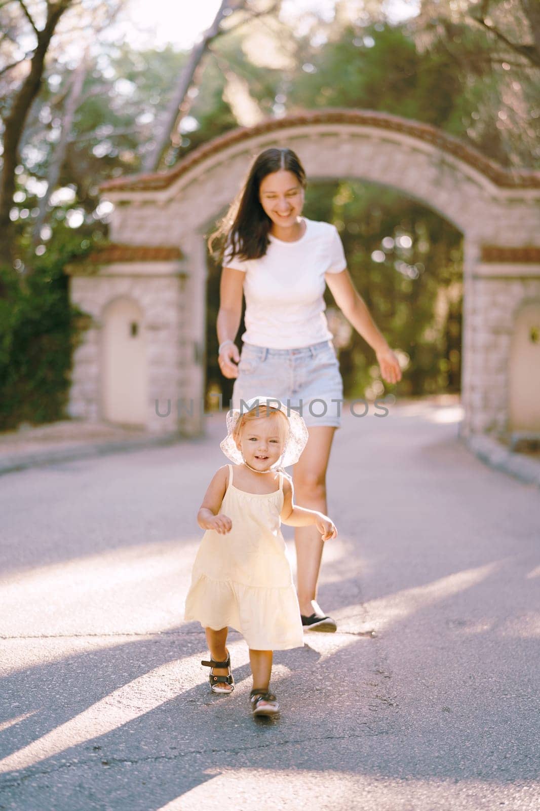 Smiling mother following her little girl along the road in the park. High quality photo