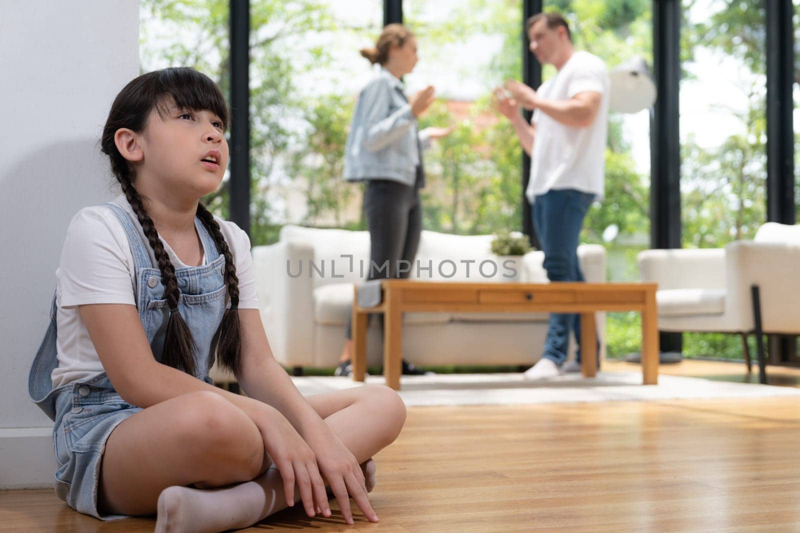 Stressed and unhappy young girl huddle in corner crying and sad while her parent arguing in background. Domestic violence at home and traumatic childhood develop to depression. Synchronos