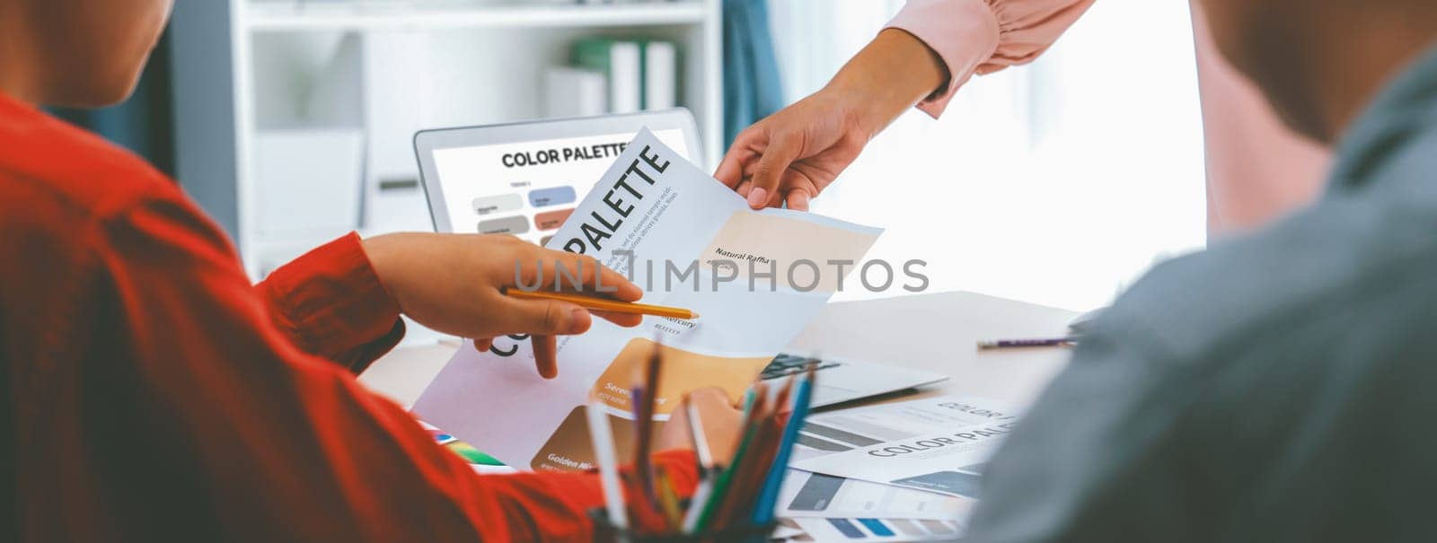 A portrait of creativity graphic designer team select appropriate color for the project by using laptop on table with equipment and designing tool scatter around at modern office. Closeup. Variegated.