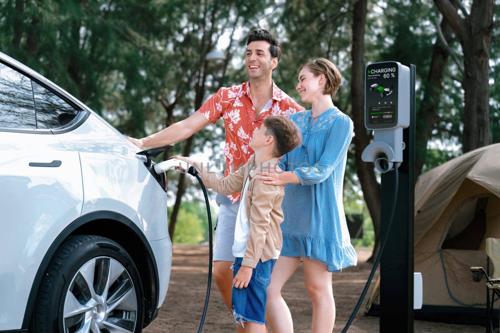 Outdoor adventure and family vacation camping in nature travel by eco friendly car for sustainable future. Lovely family recharge EV car with EV charging station in campsite. Perpetual