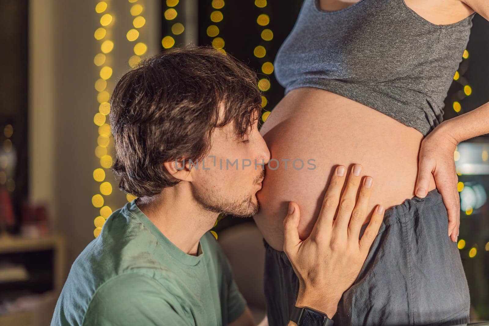 In a tender holiday moment, a husband kisses his wife's pregnant belly, expressing love and anticipation for the Christmas joy to come.