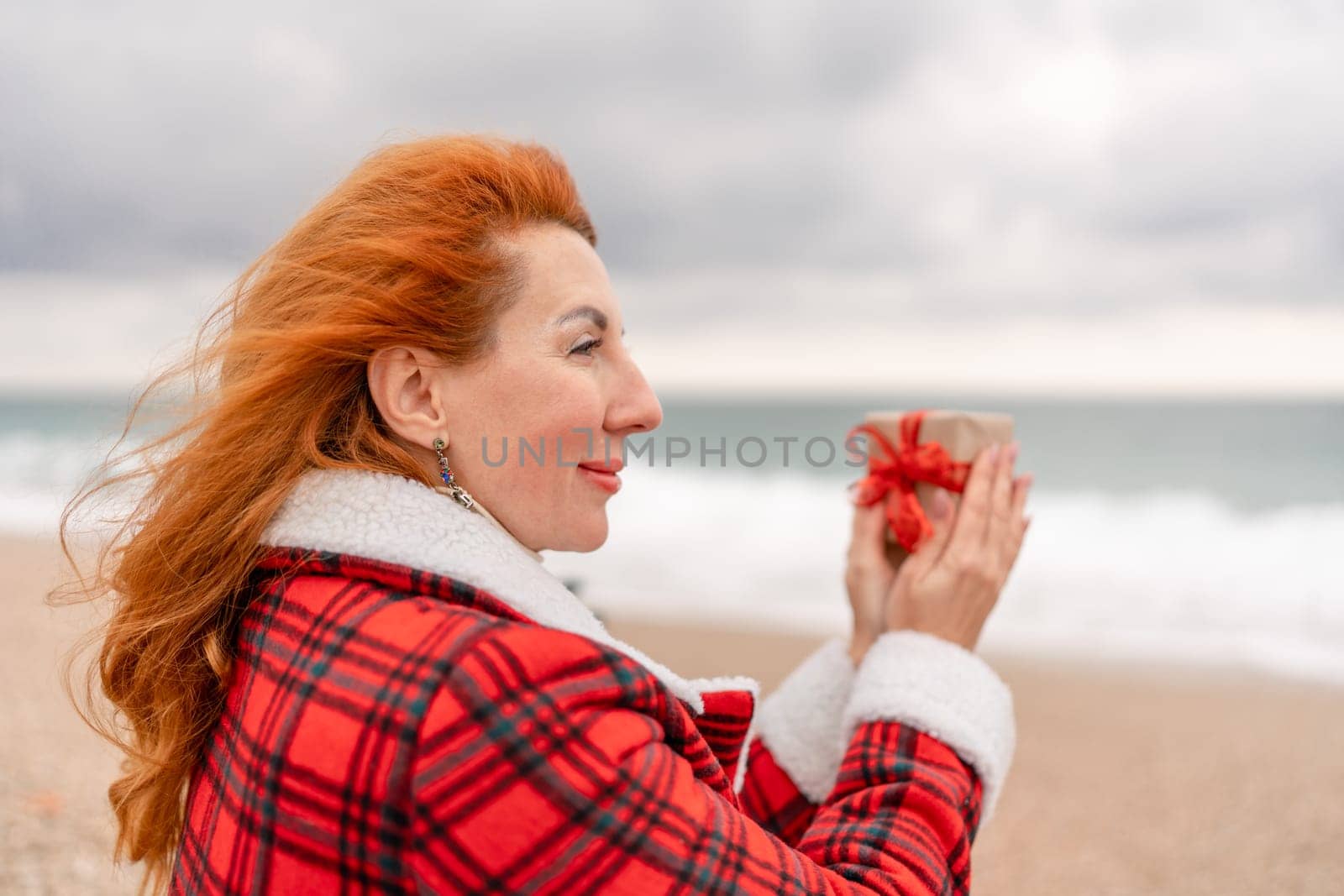 Lady in plaid shirt holding a gift in his hands enjoys beach. Coastal area. Christmas, New Year holidays concep by Matiunina