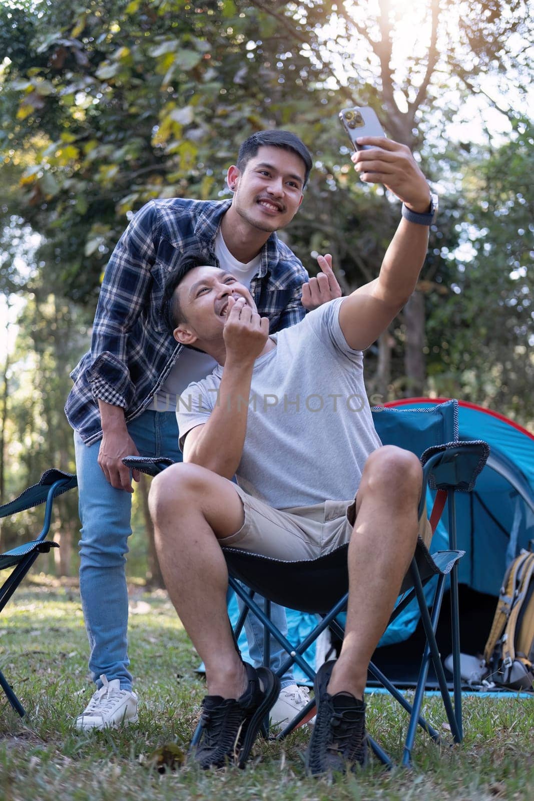 Asian LGBTQ couple tent in front of camp talking on smartphone in video chat or take a selfie by wichayada