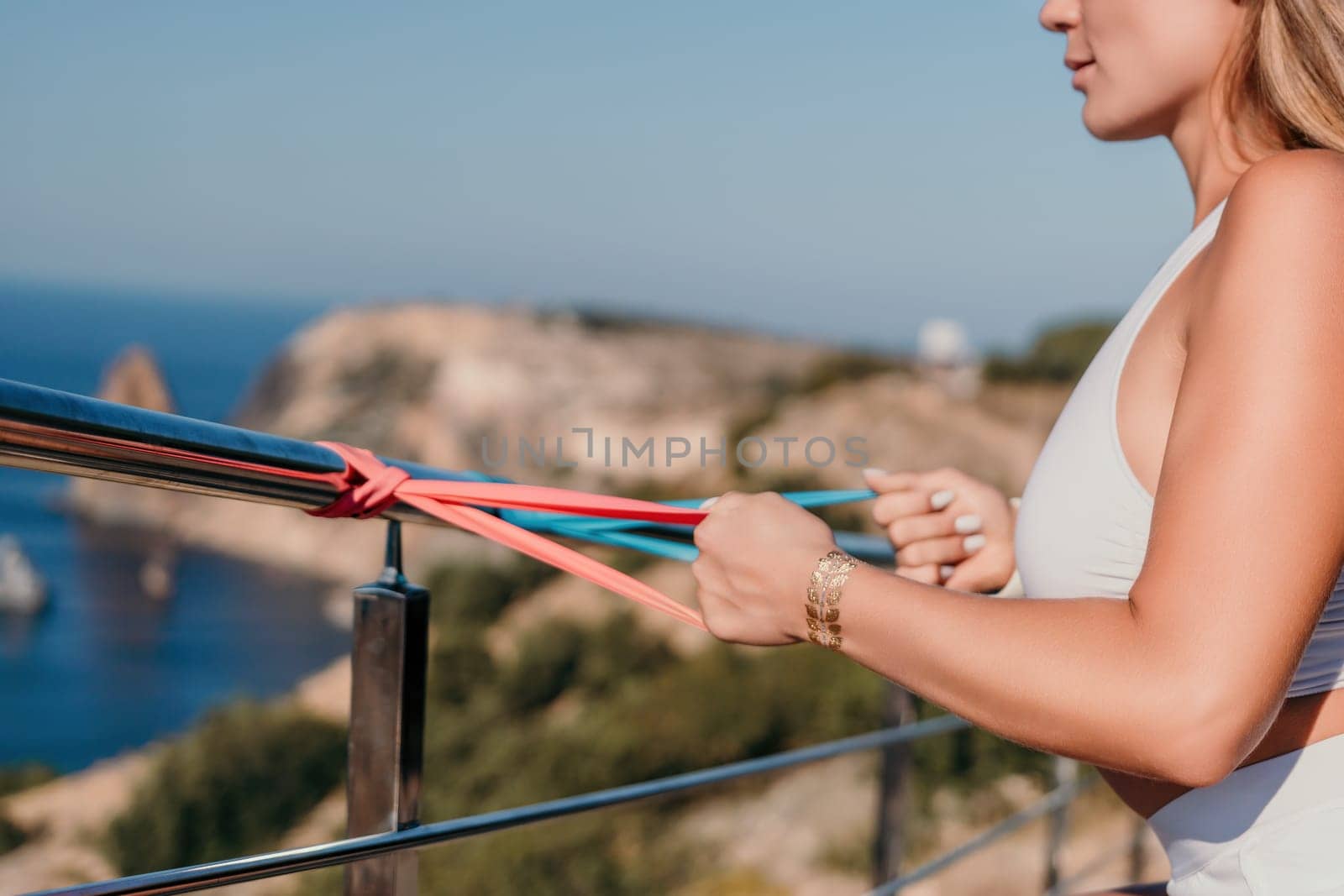 Fitness woman sea. Outdoor workout with fitness rubber bands in park over beach. Female fitness yoga routine concept. Healthy lifestyle. Happy fit woman exercising with rubber band in park. by panophotograph