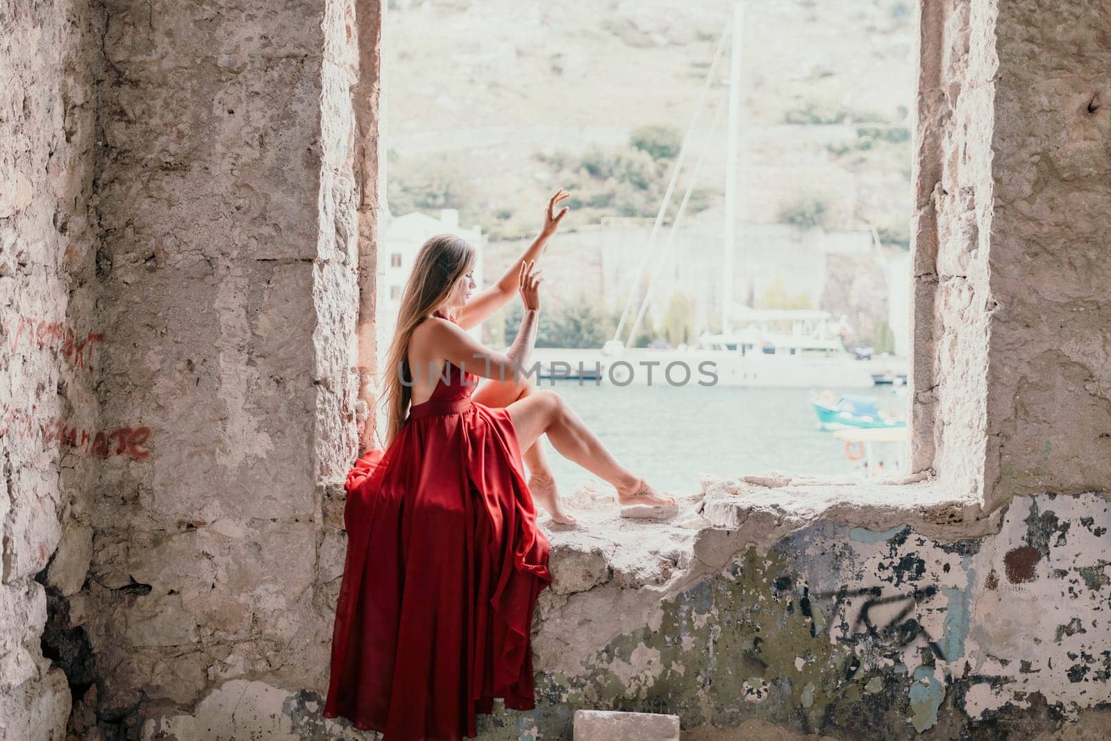 Woman travel portrait. Happy woman with long hair looking at camera and smiling. Close up portrait cute woman in a res long dress posing on backdrop of old travel city near sea by panophotograph