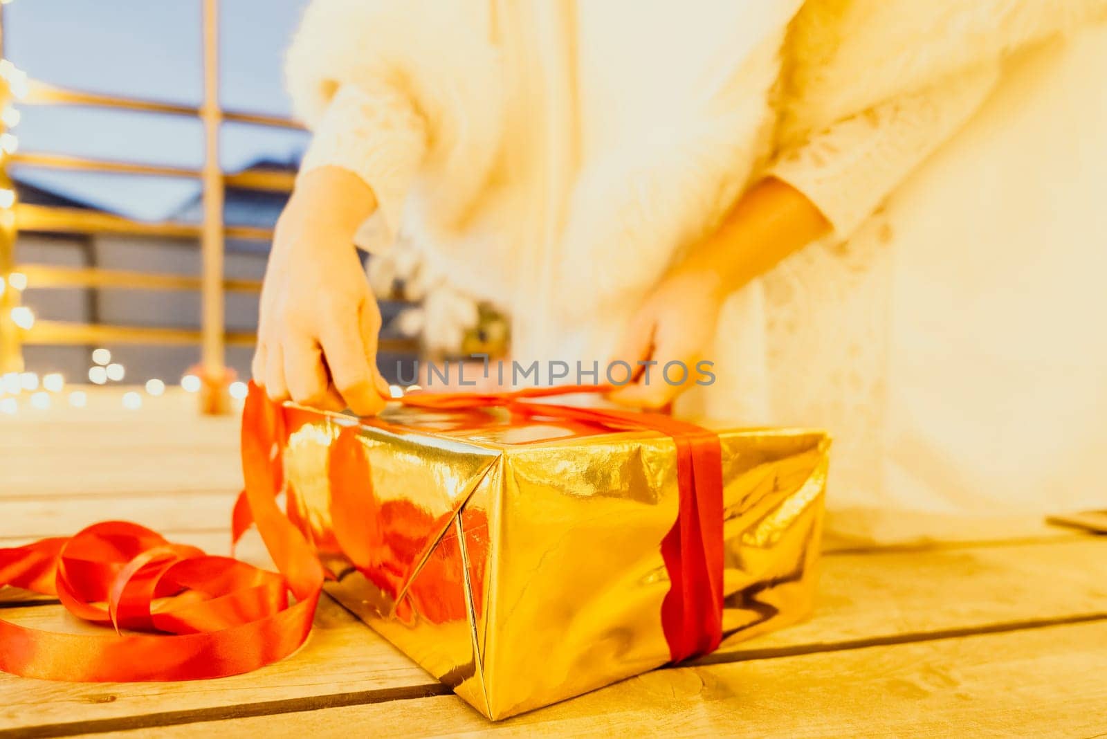 A woman in a white dress is holding a gold box with a red ribbon. She is wearing a crown on her head. The woman appears to be opening the gift box. by panophotograph