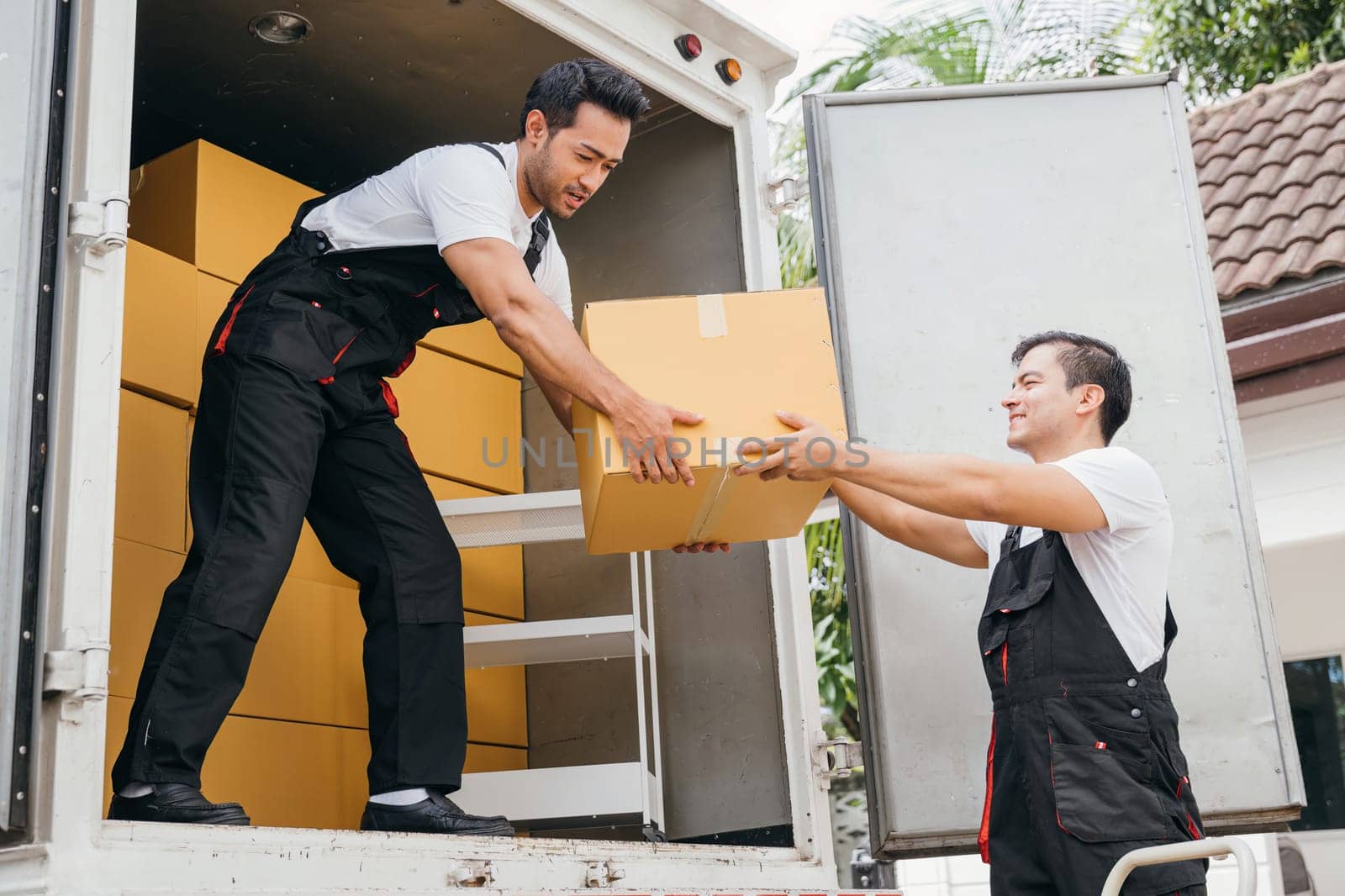 Smiling employees of a removal company work in uniform unloading boxes and furniture from the truck. Their dedication guarantees a smooth delivery into the new home ensuring happiness. Moving Day