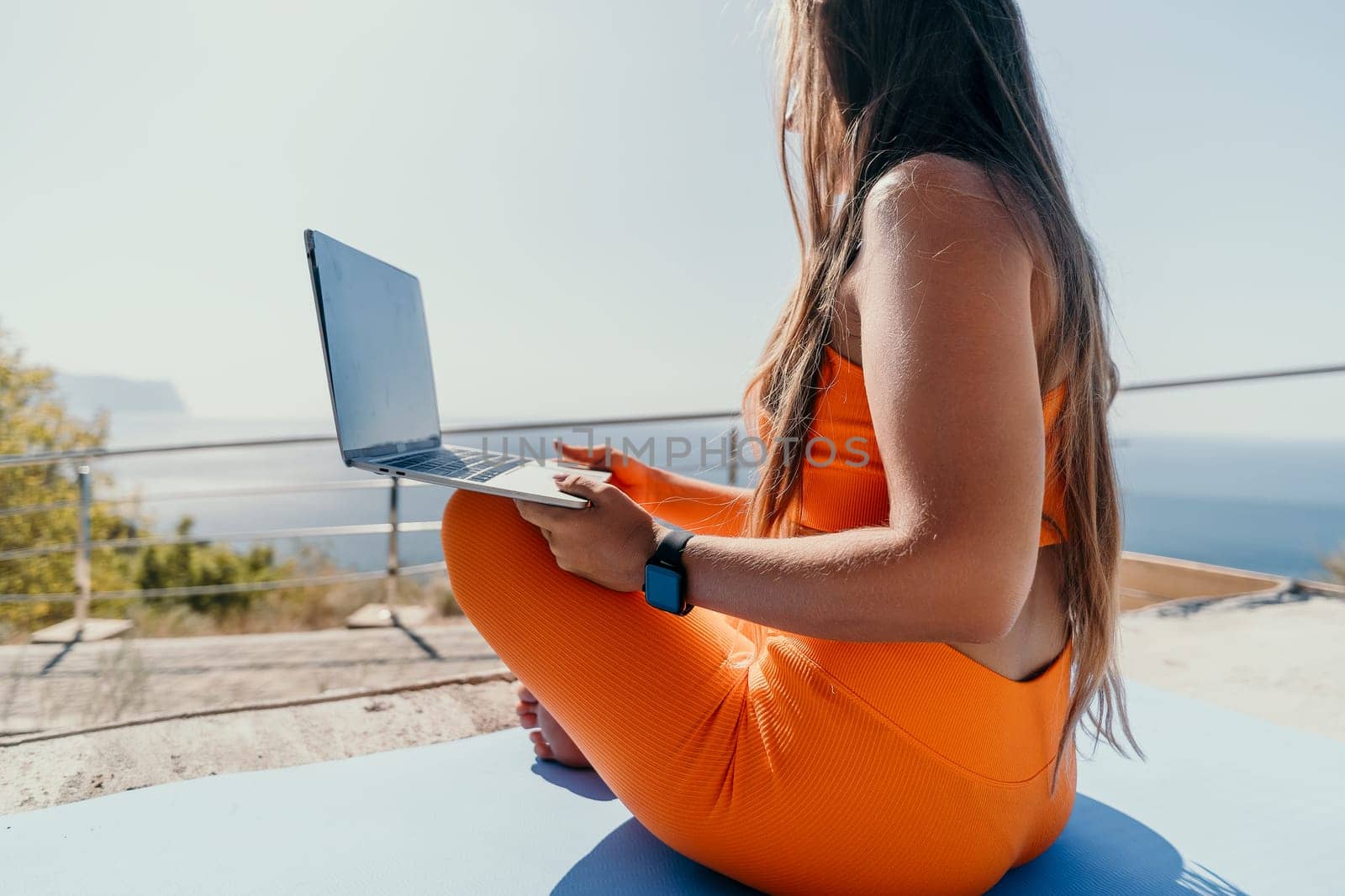 Digital nomad, Business woman working on laptop by the sea. Pretty lady typing on computer by the sea at sunset, makes a business transaction online from a distance. Freelance, remote work on vacation