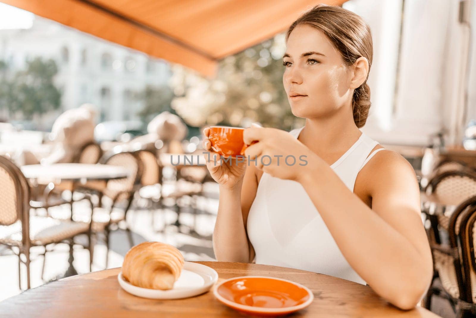 Portrait of happy woman sitting in a cafe outdoor drinking coffee. Woman while relaxing in cafe at table on street, dressed in a white T-shirt and jeans.