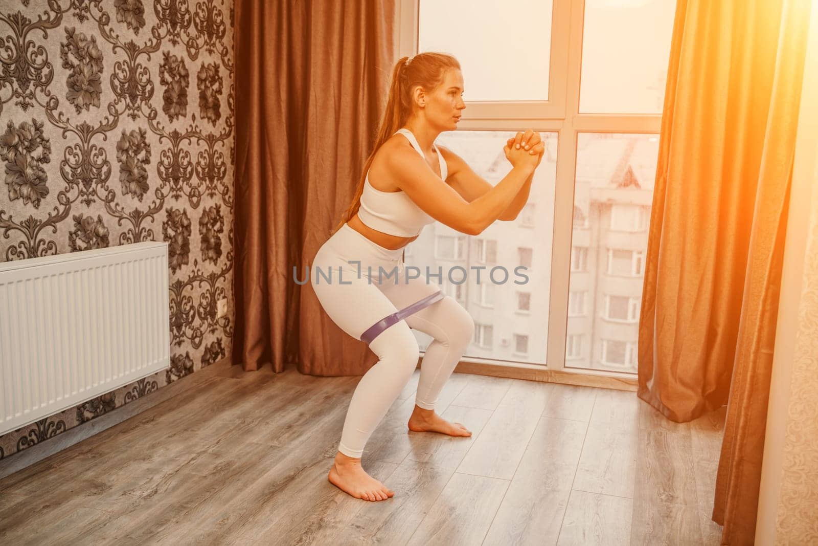 Middle aged athletic attractive woman practicing yoga. Works out at home or in a yoga studio, sportswear, white pants and a full-length top indoors. Healthy lifestyle concept by Matiunina