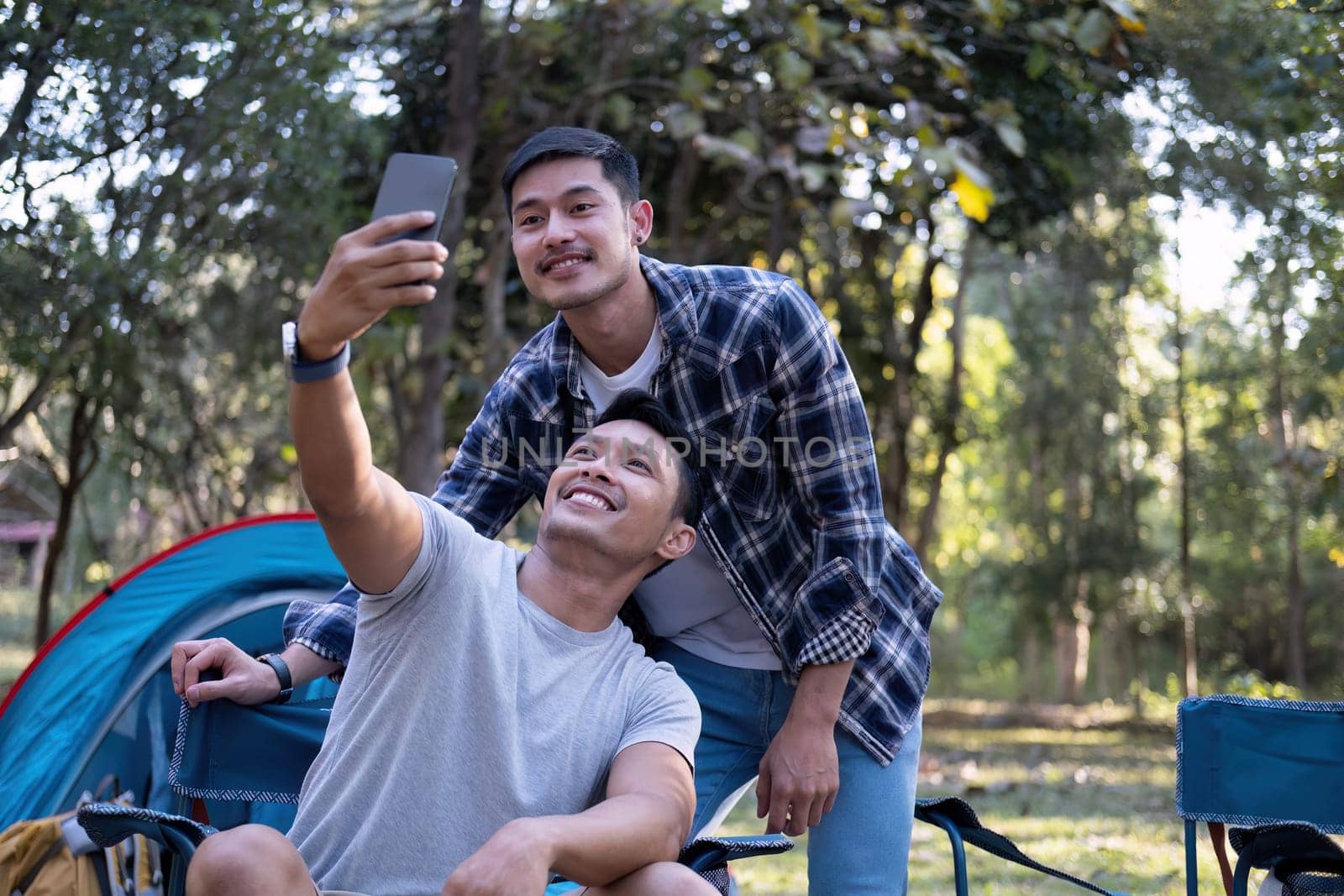 Asian LGBTQ couple tent in front of camp talking on smartphone in video chat or take a selfie by wichayada