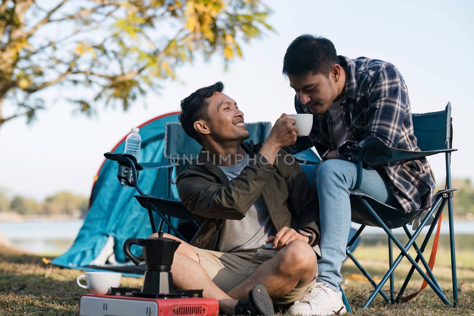 Asian LGBTQ couple drinking coffee in a romantic camping tent. LGBTQ couple drinking coffee in a camping tent, enjoying nature, forest, camping atmosphere, LGBTQ, gay, gay men. by wichayada