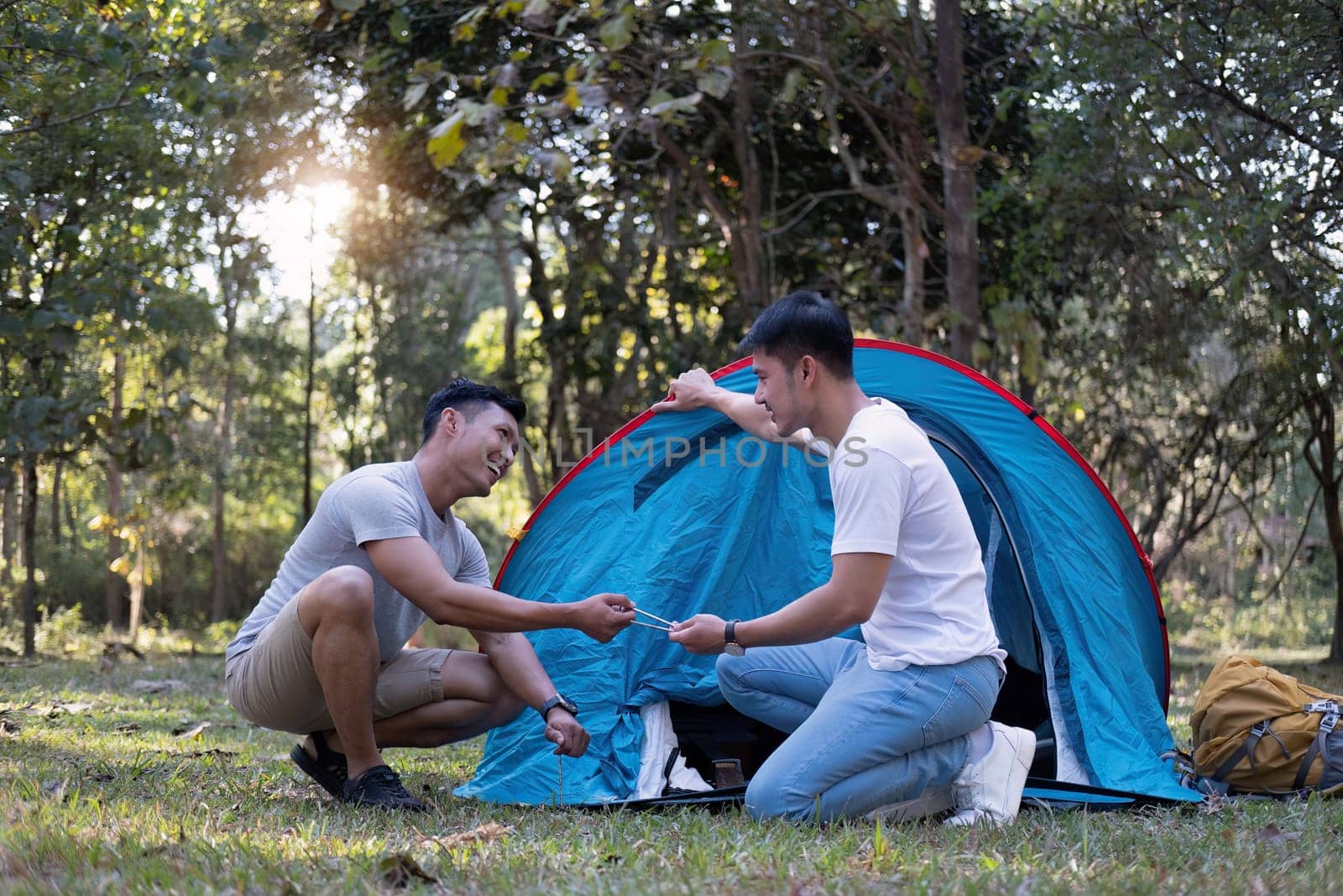 Asian LGBTQ couple camping together Set up a tent on the grass During the weekend vacation.