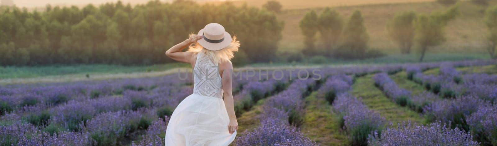 Beautiful young woman wearing a white dress walking in the middle of a lavender field in bloom.