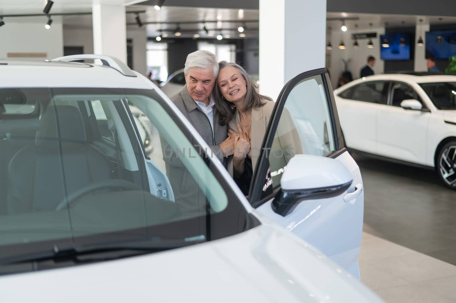 An elderly Caucasian couple chooses a new car at a car dealership. by mrwed54