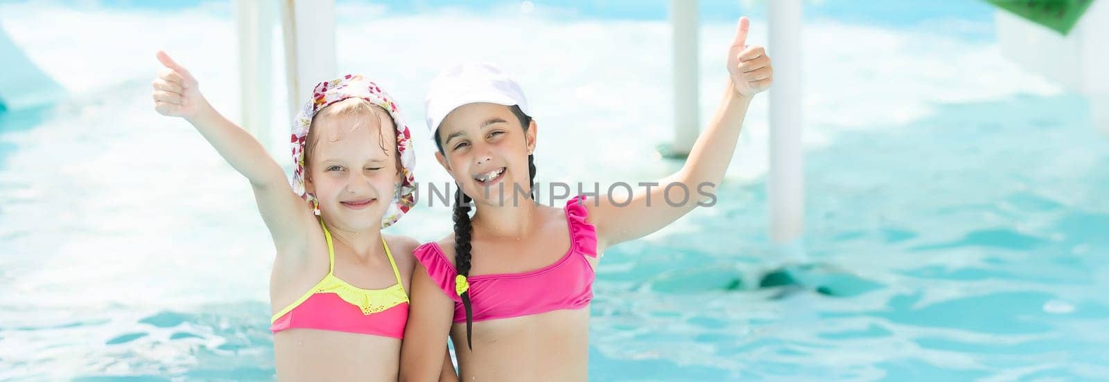 two girls splash in an outdoors swimming pool in summer. Happy children, sister playing, enjoying sunny weather in public pool.