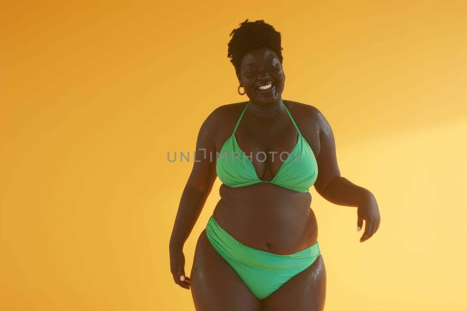 Cheerful african american looking woman in green swimsuit on bright yellow background.