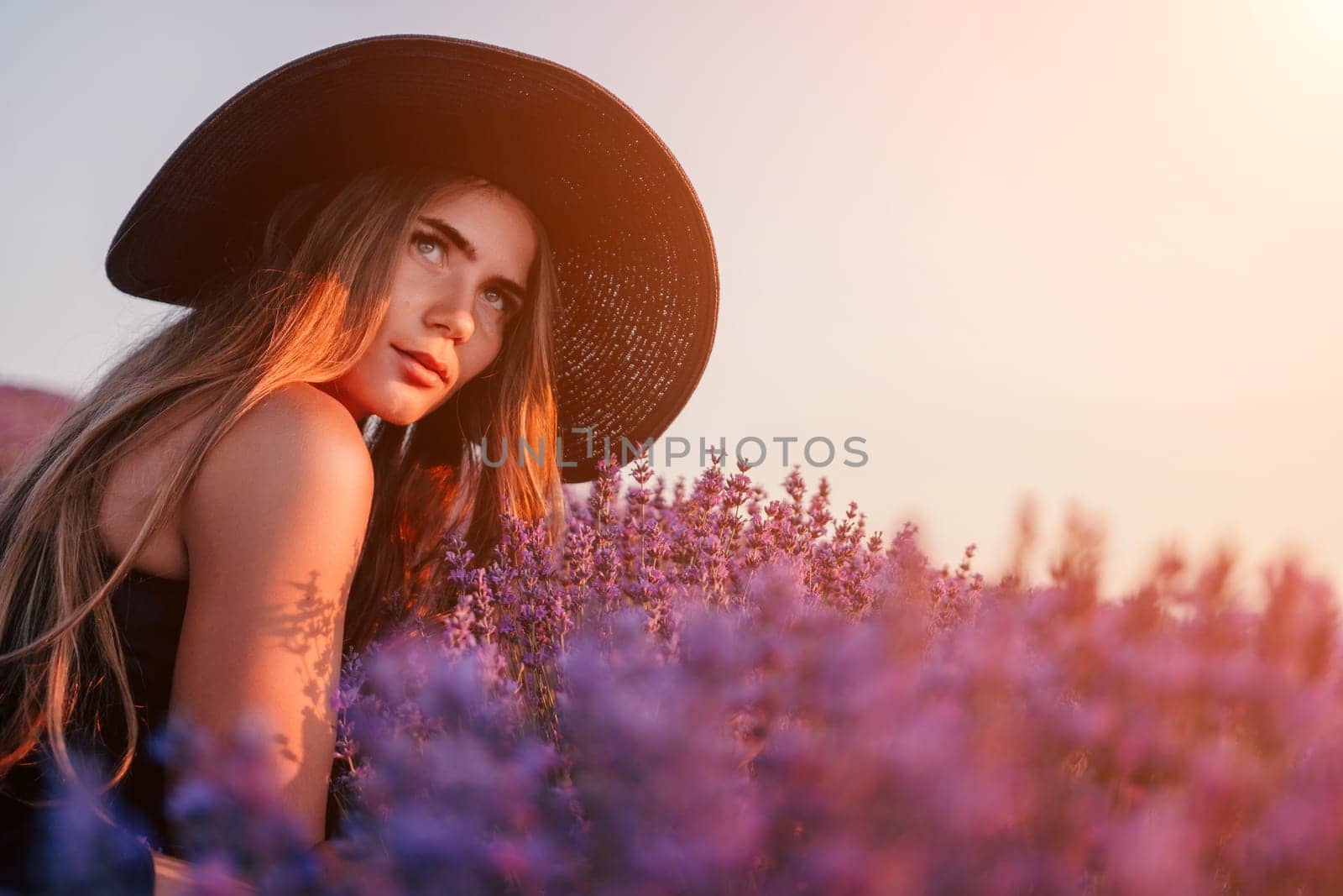 Close up portrait of young beautiful woman in a white dress and a hat is walking in the lavender field and smelling lavender bouquet.