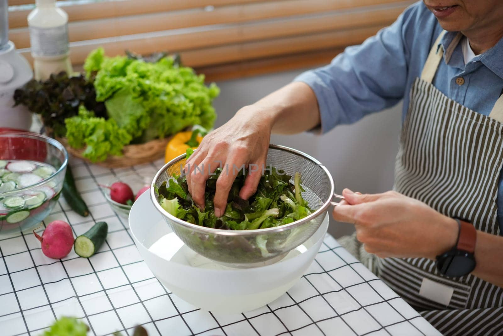 Senior man sorting out fresh vegetables preparing a fresh healthy vegan salad in kitchen by prathanchorruangsak