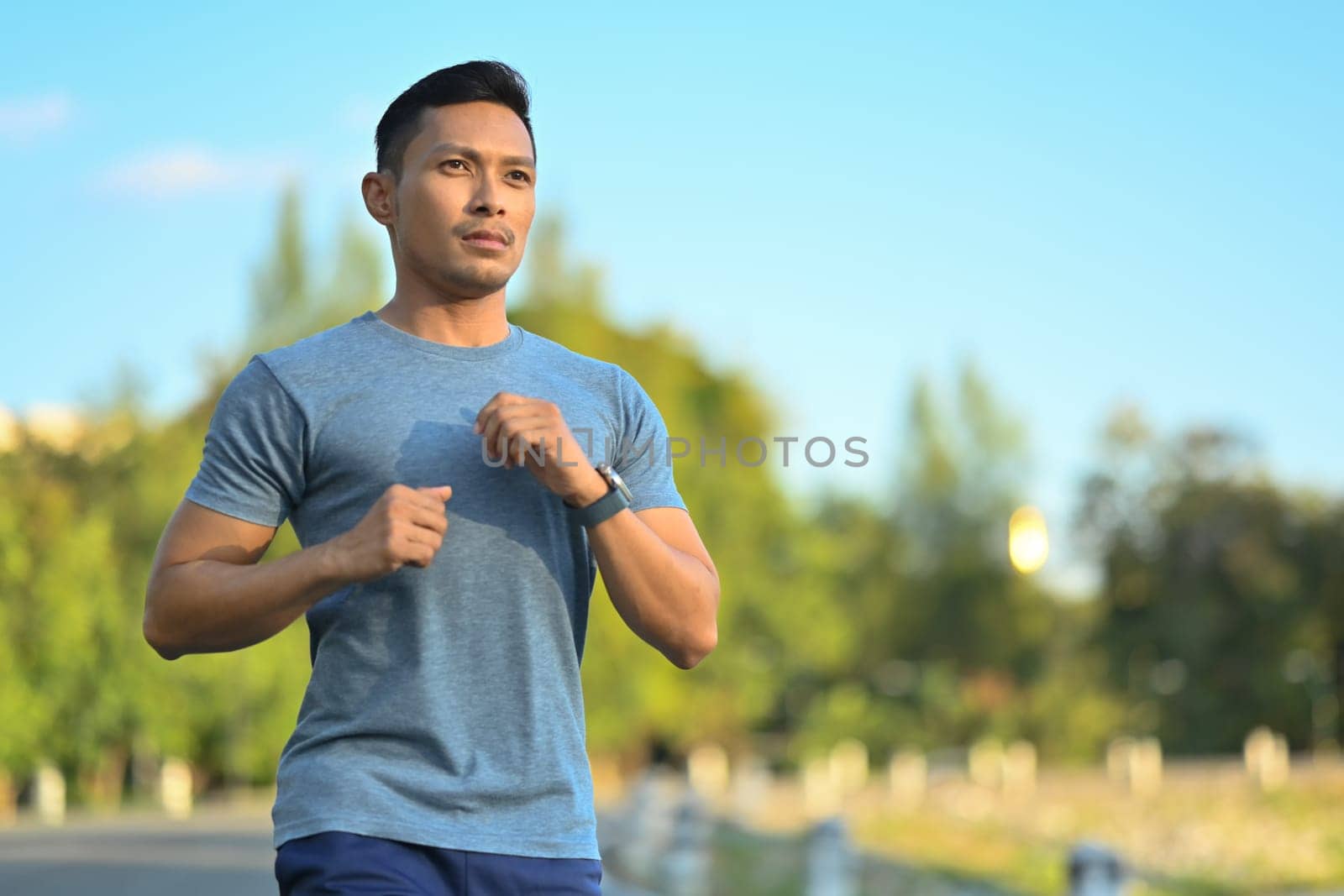 Handsome muscular sporty man jogging in the park on a sunny day. Healthy lifestyle concept. by prathanchorruangsak