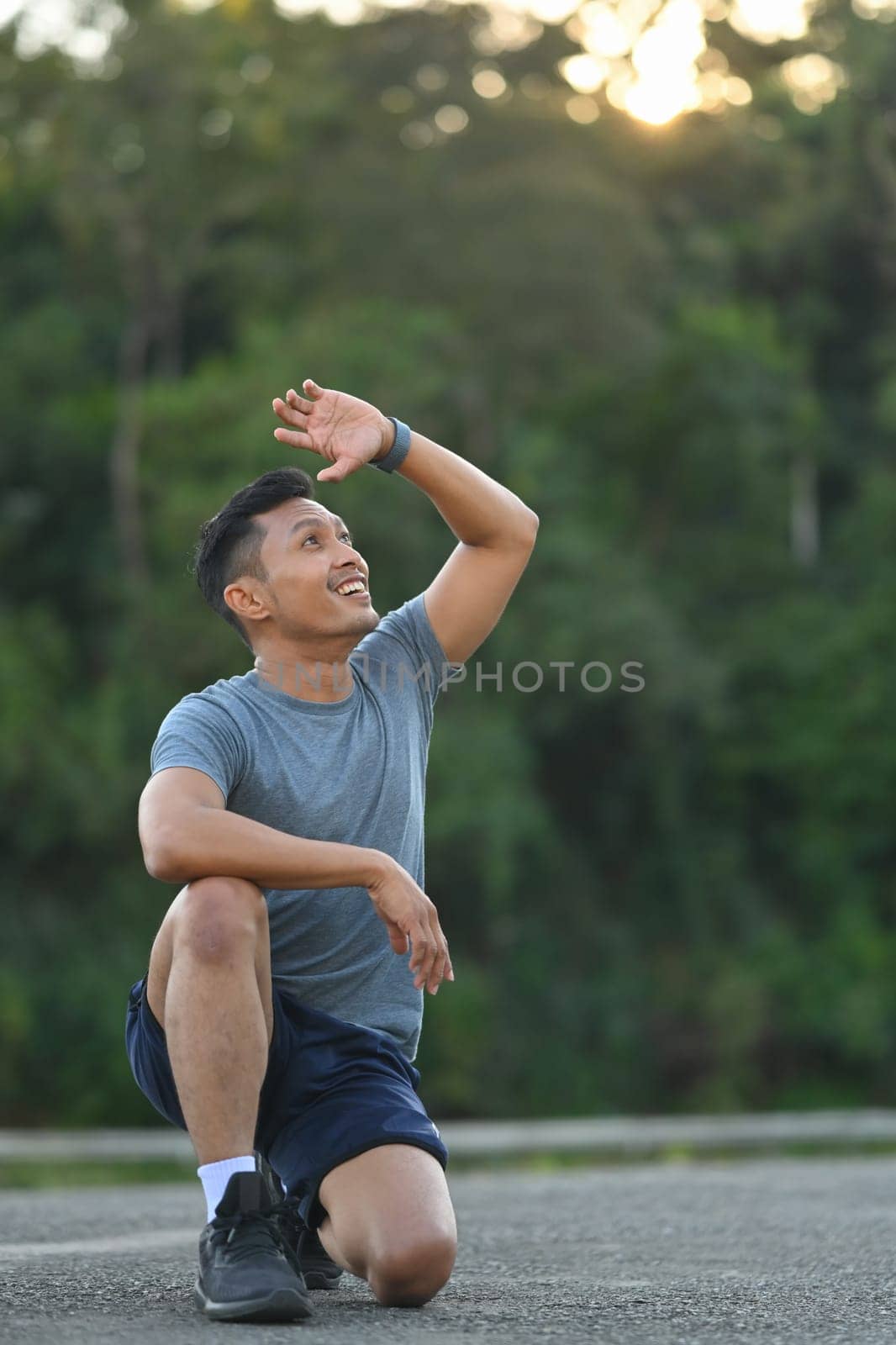 Portrait sweaty fitness male resting after workout in the park and looking away at the sunset by prathanchorruangsak