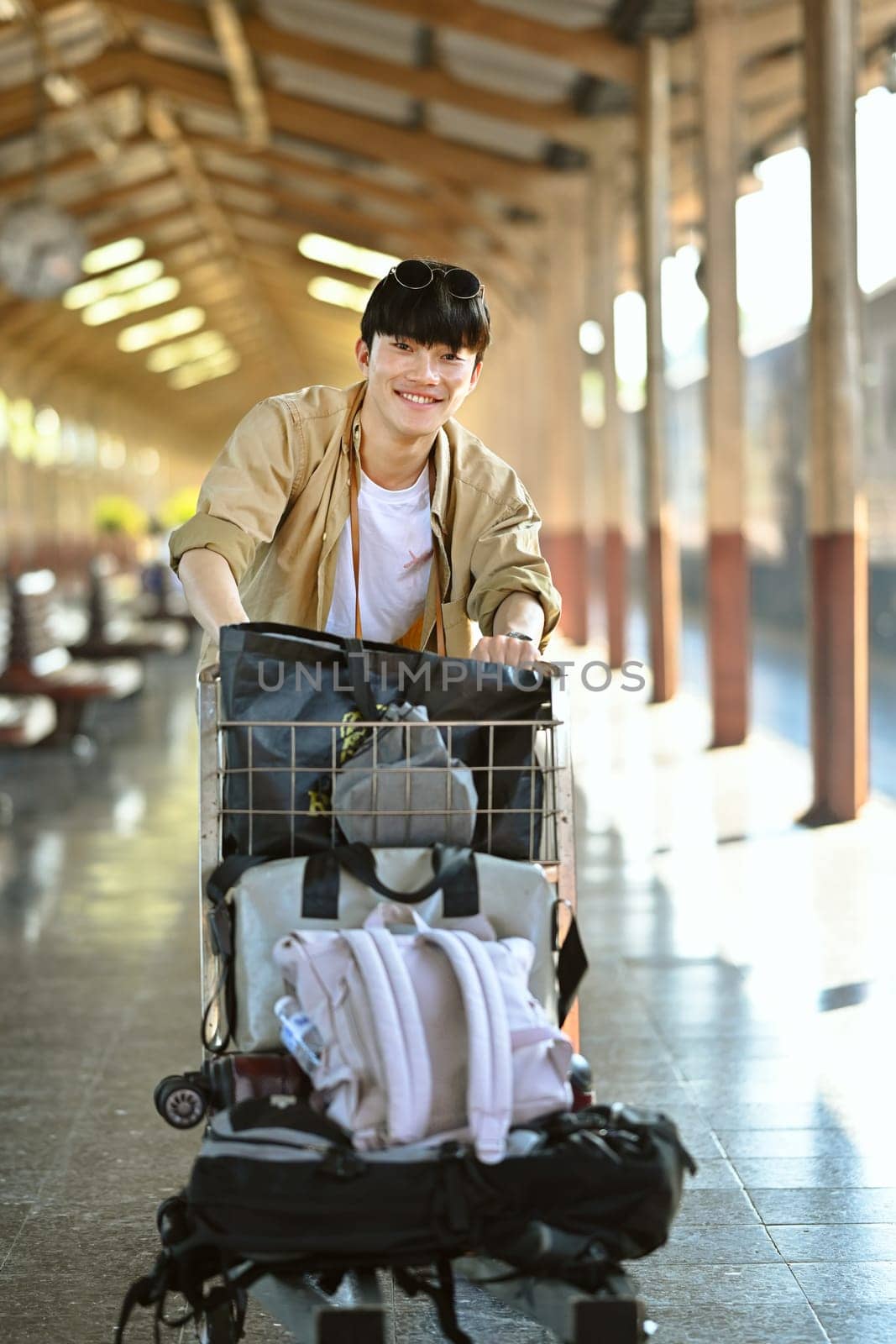 Attractive young man pushing a luggage cart walking on the corridor at railway station by prathanchorruangsak