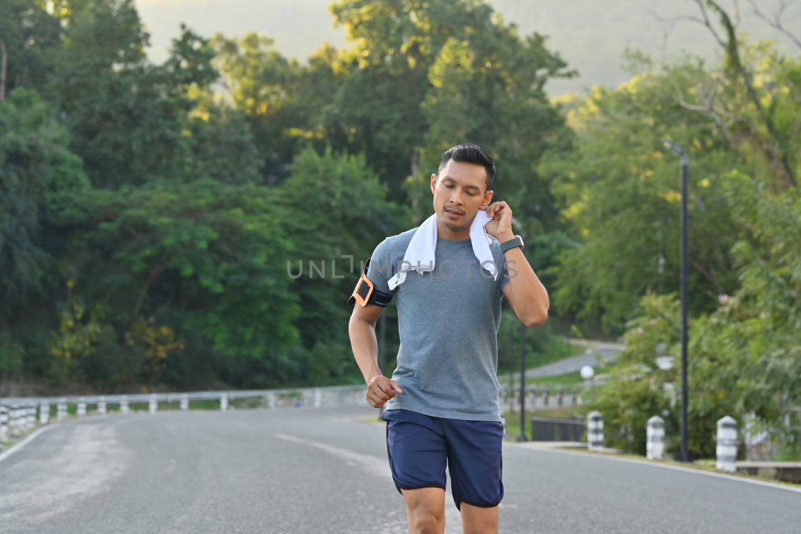 Athlete man wiping sweat from his face while running in the park. Healthy and active lifestyle concept. by prathanchorruangsak