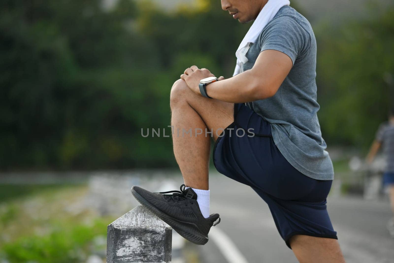 Young sportsman stretching legs in the park before running at morning by prathanchorruangsak