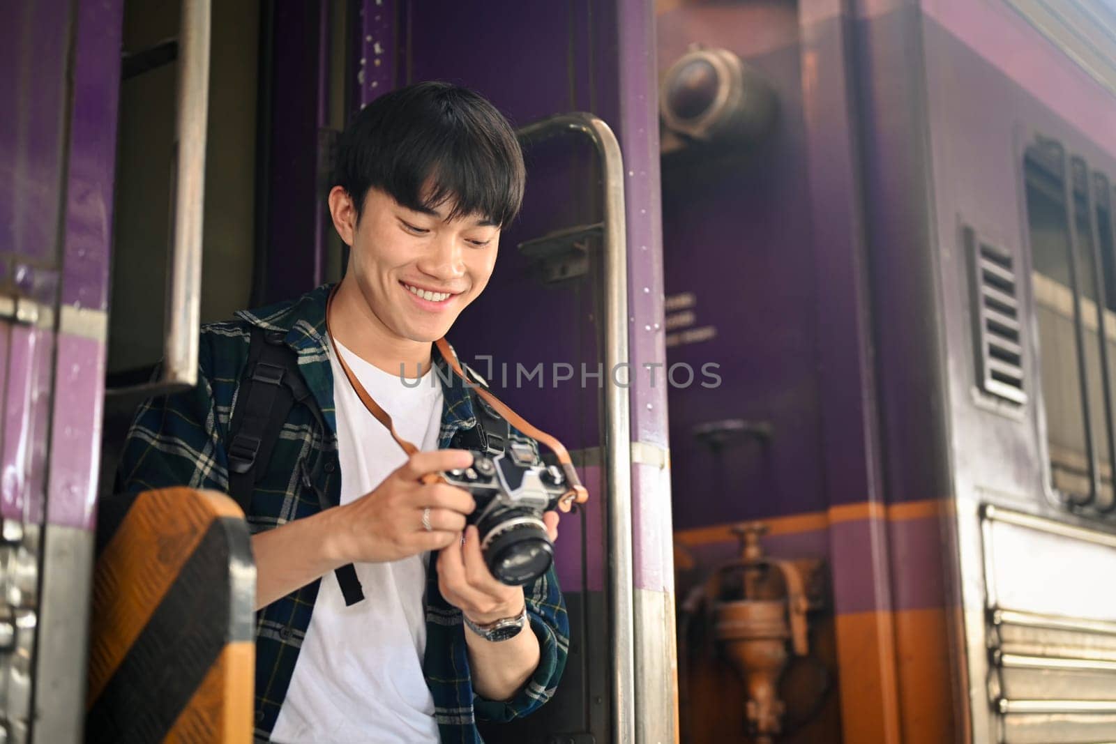 Happy male tourist with backpack checking photo on camera at the railway station.